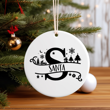 White ornament with 'Santa' design hanging on a Christmas tree.